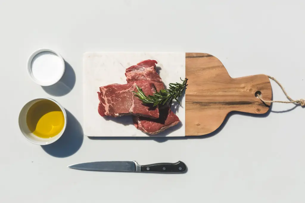 Steaks de bœuf crus sur une planche, avec huile, sel et couteau